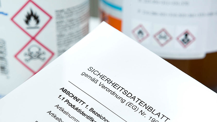 Sicherheitsdatenblatt im Vordergrund, Etiketten mit Gefahrenhinweisen im Hintergrund Sicherheitsdatenblatt im Vordergrund, Etiketten mit Gefahrenhinweisen im Hintergrund